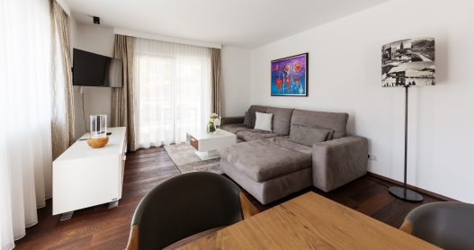Großes Wohnzimmer mit Couch, Tisch, Flatscreen TV, moderner Hifi-Anlage und Zugang zur Terrasse