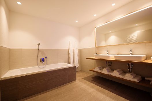 Badezimmer mit großer Badewanne, 2 Waschbecken, Handtuchtrockner, Shampoo, Duschgel und Seife