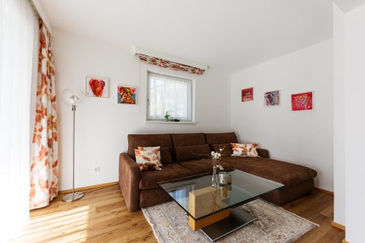 Wohnzimmer mit Couch, Tisch, Flatscreen TV, moderner Hifi-Anlage und direkter Zugang zum Garten