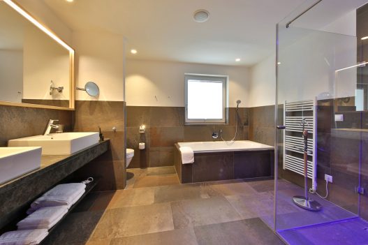 Bathroom with a large bathtub, 2 sinks, a toilet and a shower separated by glass