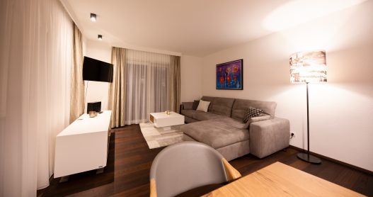 Großes Wohnzimmer mit Couch, Tisch, Flatscreen TV, moderner Hifi-Anlage und Zugang zur Terrasse