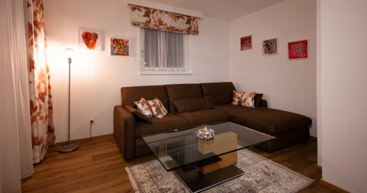 Wohnzimmer mit Couch, Tisch, Flatscreen TV, moderner Hifi-Anlage und direkter Zugang zum Garten