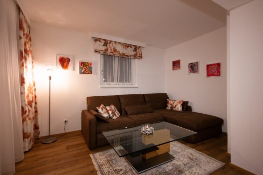 Wohnzimmer mit Couch, Tisch, Flatscreen TV, moderner Hifi-Anlage und direkter Zugang zum Garten
