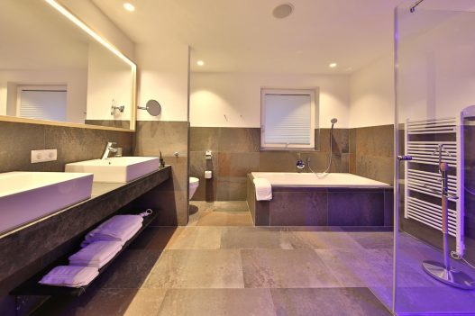 Bathroom with a large bathtub, 2 sinks, a toilet and a shower separated by glass