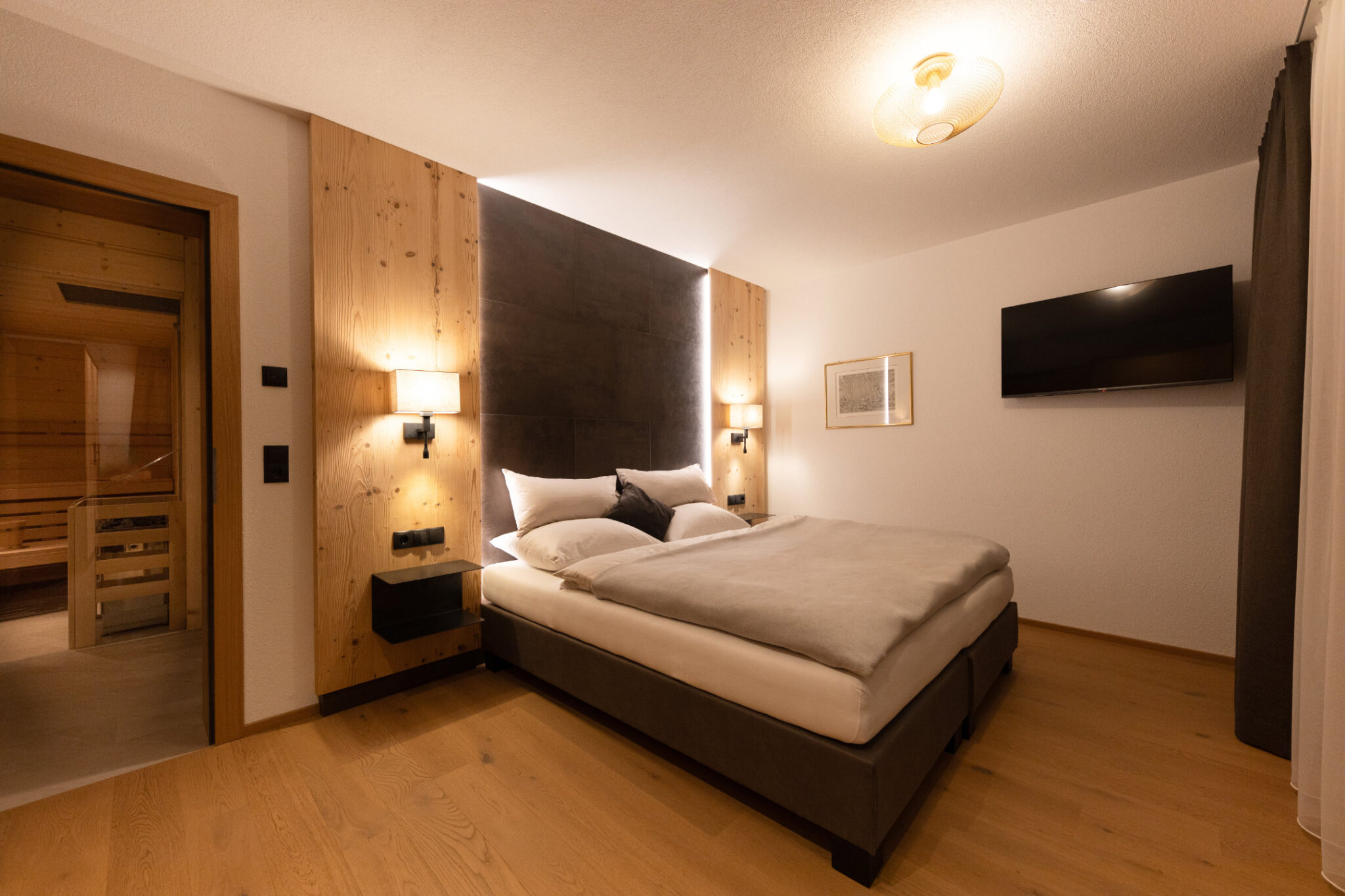 Schlafzimmer Erdgeschoss Ost mit Doppelbett, Nachttischen, Fernseher und Fenster – Mountain Chalet da Peatala Apartments Serfaus Winter