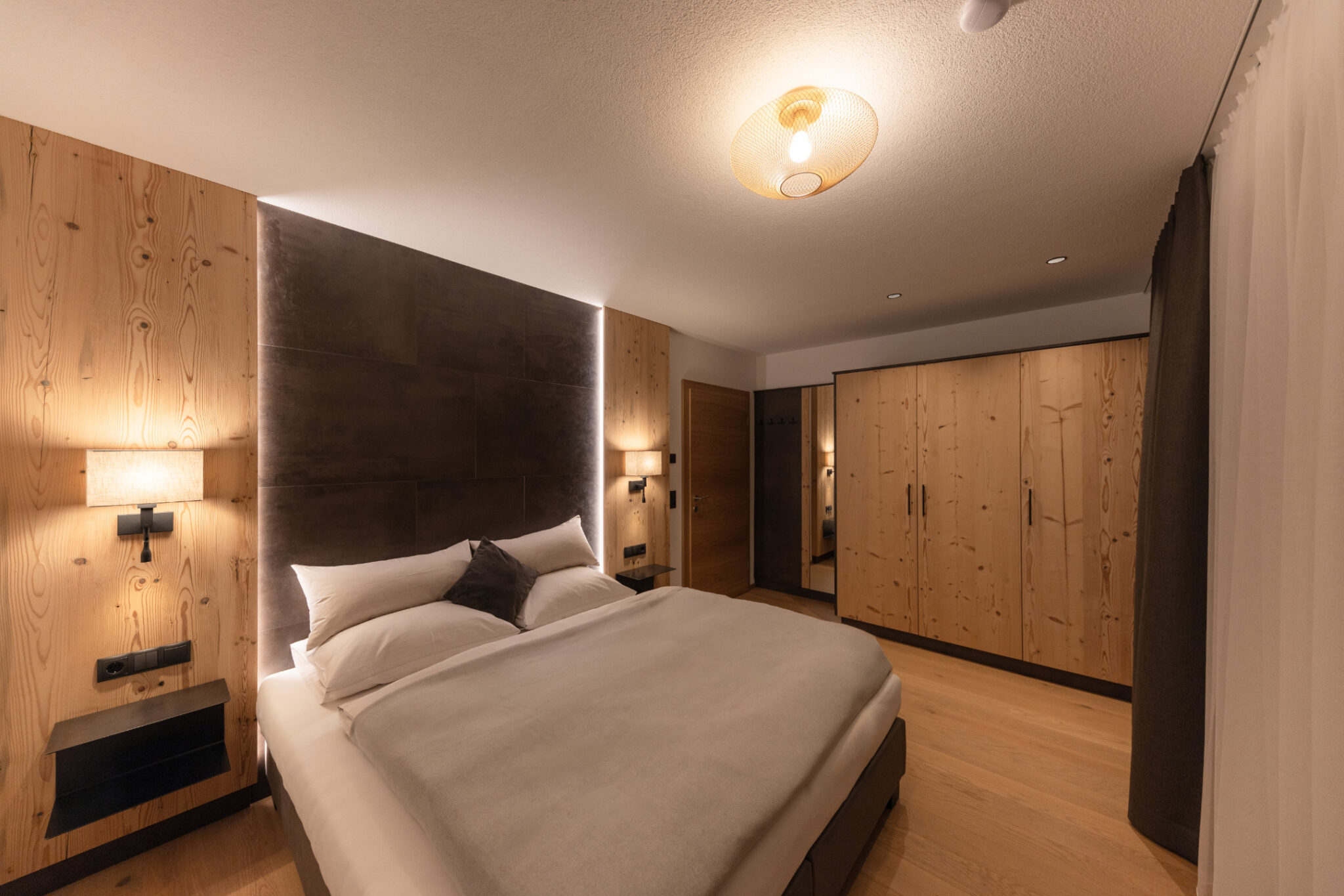 Schlafzimmer Erdgeschoss West mit Doppelbett, Nachttischen und Fenster – Mountain Chalet da Peatala Apartments Serfaus Winter